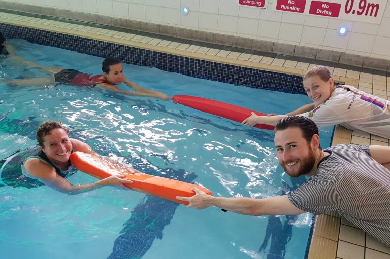 People in a pool participating in a life saving course with flotation devices.