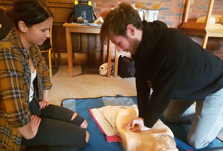 A man performs CPR on a training dummy while a woman observes attentively.